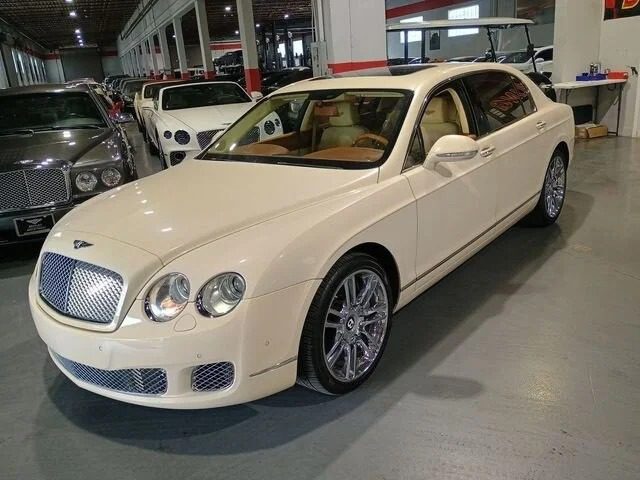 A white Bentley sedan is parked in an indoor showroom with other luxury sedans in the background, highlighting a stunning selection of sedans for sale.
