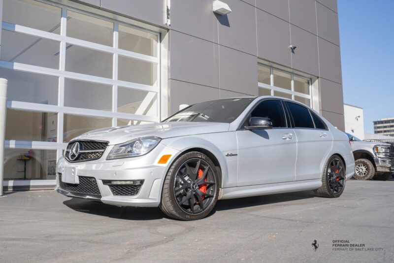 A silver Mercedes-Benz C63 AMG sedan with black wheels and red brake calipers, parked outside a modern building, showcases the pinnacle of affordable luxury sedans.