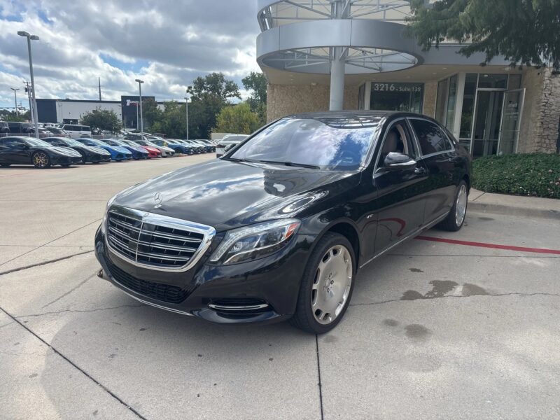 A black Mercedes-Benz sedan, an excellent choice among affordable luxury cars, is parked in front of a building on a concrete lot, with other vehicles visible under a partly cloudy sky.
