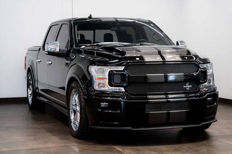 A black Shelby-modified Ford F-150 pickup truck from Shelby Trucks is parked indoors on a polished floor, facing slightly to the left—ready and available for sale.