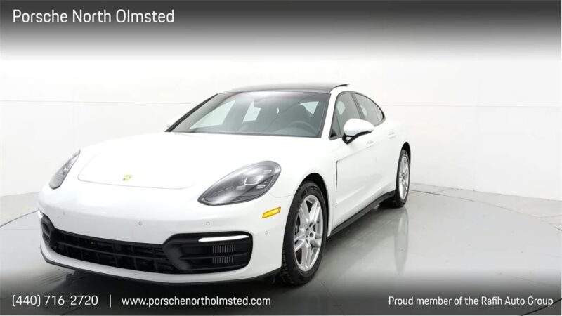 A white Porsche sedan is displayed in a showroom with the Porsche North Olmsted dealership information at the bottom, offering one of the finest luxury sedans for sale.