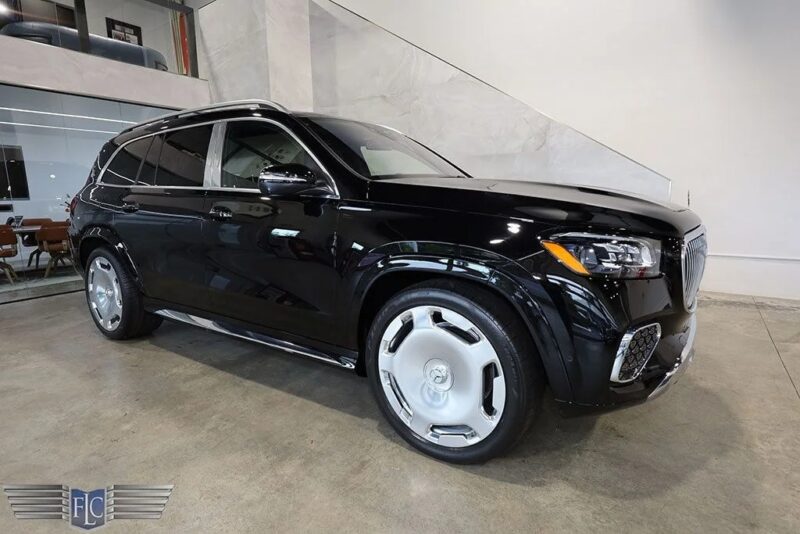 A black Mercedes-Benz SUV with chrome accents and large silver wheels is parked indoors on a polished concrete floor near a glass-walled office, showcasing this luxury car for sale.