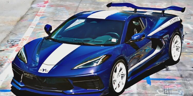 A blue Yenko C8 Corvette sports car with white racing stripes and a large rear spoiler is parked on a graffiti-covered road.