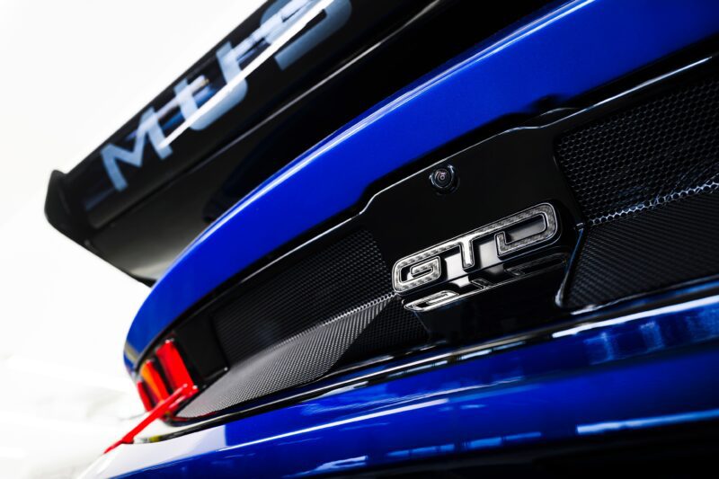 Primer plano de la parte trasera de un automóvil azul, que muestra la insignia GTD, el alerón negro y parte de la luz trasera, haciendo eco del músculo pony máximo visto en la primera conducción: Ford Mustang GTD de seis cifras.