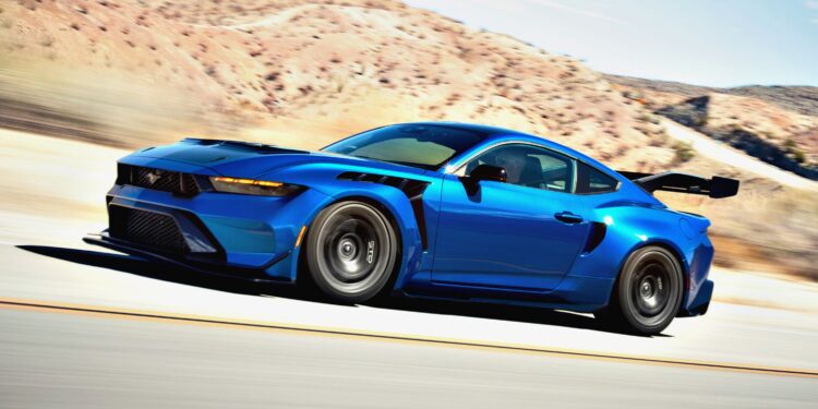 Primer manejo: un Ford Mustang GTD de seis cifras presume de su máximo poderío mientras un auto deportivo azul con un gran alerón trasero avanza por la carretera, con montañas elevándose en el fondo.