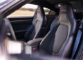 The image shows the black front seats of a sports car with "GTS" embroidered on the headrests and a center console in between, capturing the refined interior featured in the Review: 2025 Porsche 911 Carrera GTS T-Hybrid Electrifies Potent Performance.