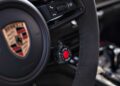 Close-up of a Porsche steering wheel showing the logo and a drive mode selector knob with a red "Drive Mode" label—highlighting features from the Review: 2025 Porsche 911 Carrera GTS T-Hybrid Electrifies Potent Performance.