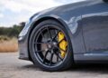 Close-up of the front wheel of a grey Porsche sports car with yellow brake calipers and "t-hybrid" badge, as seen in the review: 2025 Porsche 911 Carrera GTS T-Hybrid electrifies potent performance.
