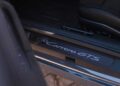 Close-up view of a car door sill with "Carrera GTS" lettering, next to a black leather seat with visible stitching. Review: 2025 Porsche 911 Carrera GTS T-Hybrid electrifies potent performance.