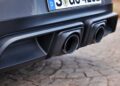 Close-up of the 2025 Porsche 911 Carrera GTS T-Hybrid’s rear, showcasing dual black exhaust pipes and part of a license plate, parked on a paved surface. Review: This electrifies potent performance in every detail.