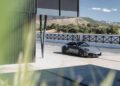 A black 2025 Porsche 911 Carrera GTS T-Hybrid is parked near a modern building, with mountains and trees in the background under a clear sky—review: this electrifies potent performance in an elegant setting.