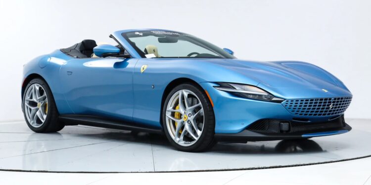 A blue convertible exotic car with the top down, featuring alloy wheels and yellow brake calipers, displayed in a white studio setting.