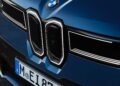 Close-up of the front grille and badge of a blue BMW car, showing part of the license plate and sleek headlight design, as BMW iX3 launches the Neue Klasse Era with 400-mile range and 463 HP.