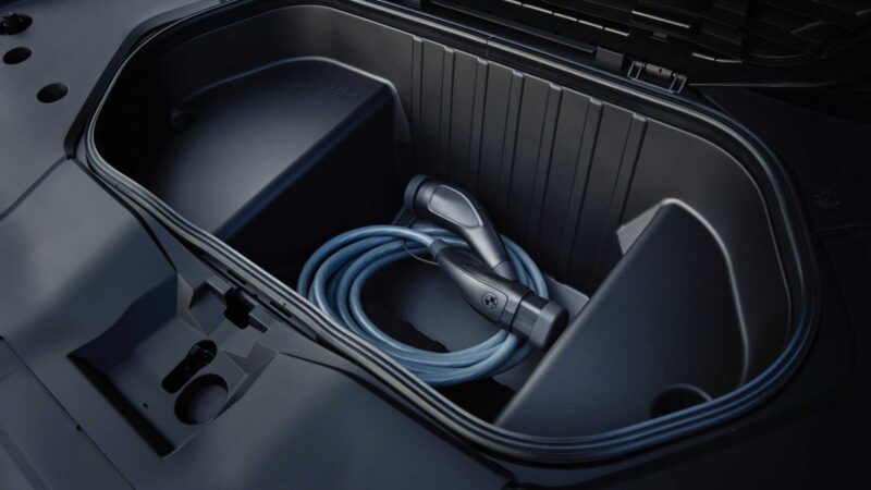 An electric vehicle charging cable is neatly stored in the front trunk compartment of a car, ready for use with models like the BMW iX3, which launches the Neue Klasse era with a 400-mile range and 463 HP.