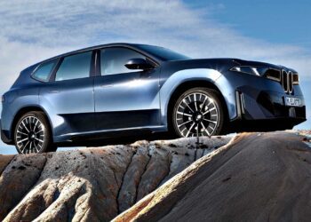 A blue BMW SUV, embodying the BMW iX3 Launches the Neue Klasse Era With 400-Mile Range and 463 HP, is parked on rocky terrain under a clear sky, viewed from a side angle.