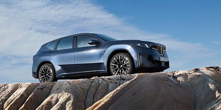 A silver SUV is parked on rocky terrain under a blue sky with scattered clouds.