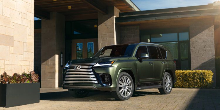 A green Lexus SUV is parked on a stone driveway in front of a modern house with large windows and stone walls.