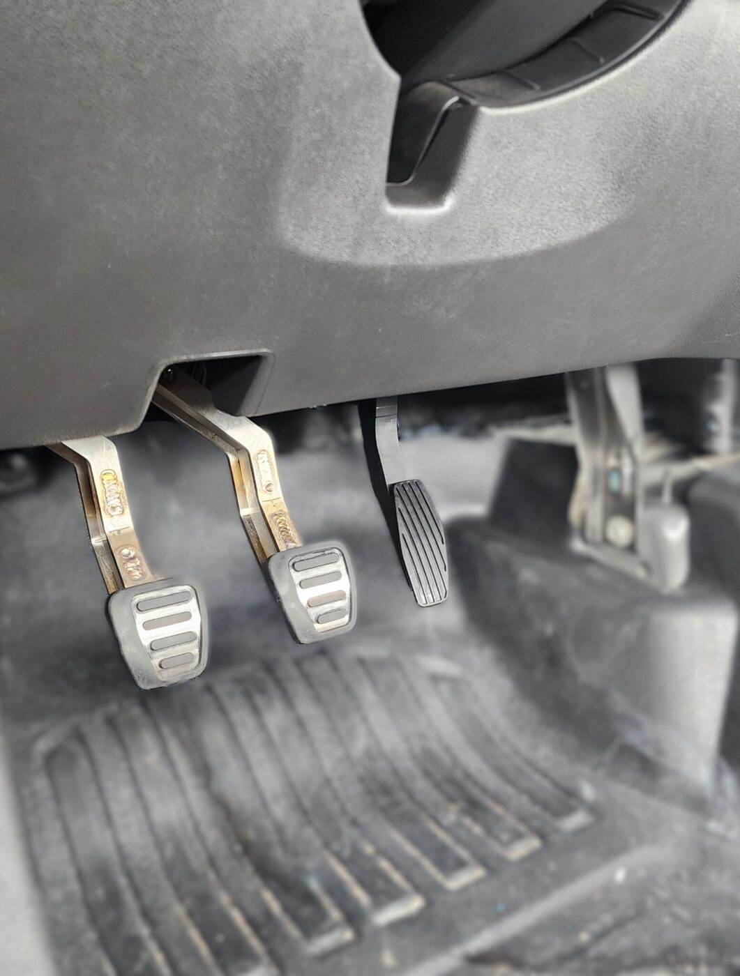 Close-up view of the clutch, brake, and accelerator pedals in a YENKO Silverado’s footwell, with a rubber floor mat visible beneath—highlighting this supercharged truck’s driver-focused details.