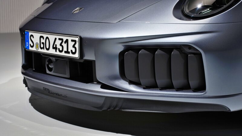 Close-up of the front bumper and license plate of a silver 2026 Porsche 911 Turbo S T-Hybrid, the most powerful production 911, showcasing headlight, grille, aerodynamic details, and its impressive 701HP performance.