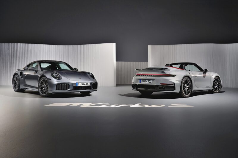 Two Porsche 911 Turbo S cars, including the Most Powerful Production 911: 2026 Porsche 911 Turbo S T-Hybrid with 701HP, are displayed in a studio with a minimal white background.