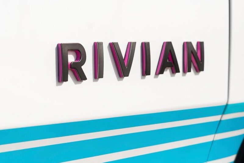 Close-up of the Rivian logo on a white vehicle with blue diagonal stripes, celebrating as Rivian opens Brickell Hub with a one-off Miami-themed tri-motor R1S.