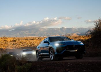 Three SUVs, including a Lamborghini Urus SE, drive on a dusty dirt road through a desert landscape near Zion National Park, with mountains and clouds in the background.