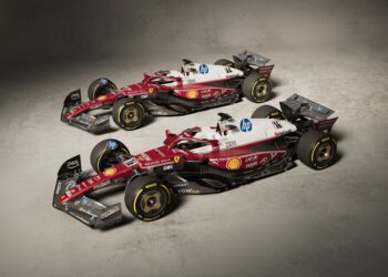 Two Formula 1 cars with red, white, and black livery are parked side by side on a concrete floor, displaying sponsorship logos including Shell, HP, and IBM.