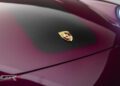 Close-up of a Porsche emblem on the hood of a burgundy Gunther Werks Speedster with a carbon fiber insert, highlighting Graham Rahal Performance details.