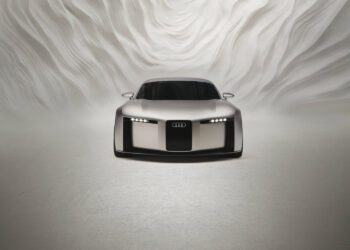 A silver Audi concept sports car is shown from the front in a minimalistic, white setting with abstract, wavy wall patterns in the background.