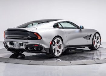 A silver Aston Martin coupe from Galpin Aston Martin is displayed on a rotating platform, viewed from the rear three-quarter angle in a studio setting—an exquisite choice among exotics for sale.