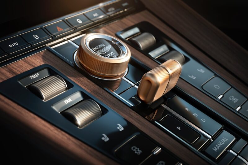 Close-up of a car's central control panel with a start/stop engine button, drive mode selector, climate controls, and gear shift on wood finish—reflecting the bespoke elegance of Q by Aston Martin Marks 60 Years of Volante With Ultra-Exclusive Anniversary Editions.