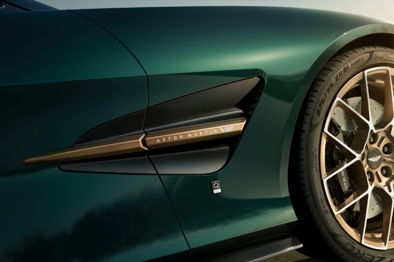 Close-up of a green Aston Martin V12 sports car, showcasing the front wheel, side vent, and gold accent with branding detail—part of the ultra-exclusive Q by Aston Martin Marks 60 Years of Volante Anniversary Editions.