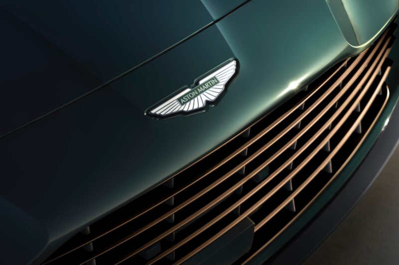 Close-up of an Aston Martin car front grille with the silver Aston Martin logo, celebrating Q by Aston Martin Marks 60 Years of Volante With Ultra-Exclusive Anniversary Editions.