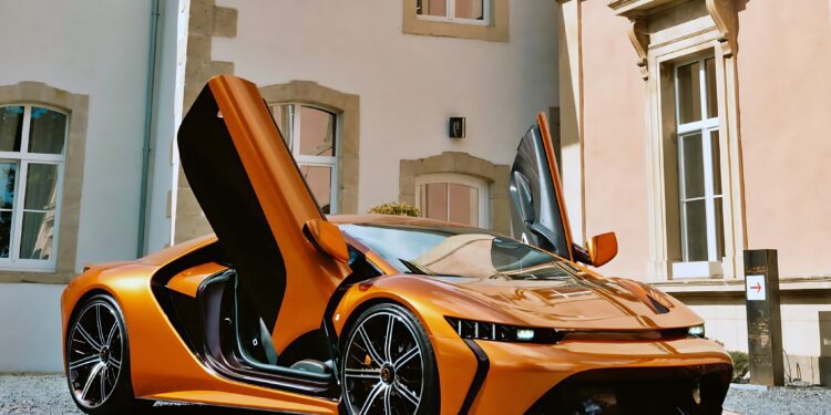 An orange Bertone GB110 meets Arancio Zero—a color that defined an era—with its scissor doors open, parked on a gravel surface in front of a beige building with large windows.