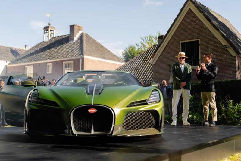 A green 1-of-1 Bugatti Brouillard makes its European debut at Wheels Mariënwaerdt, displayed on an outdoor stage with several people nearby, set against traditional European-style buildings.