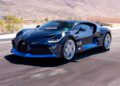 A blue carbon Bugatti Divo speeds along a paved road, set against a mountainous desert landscape, and is now for sale.