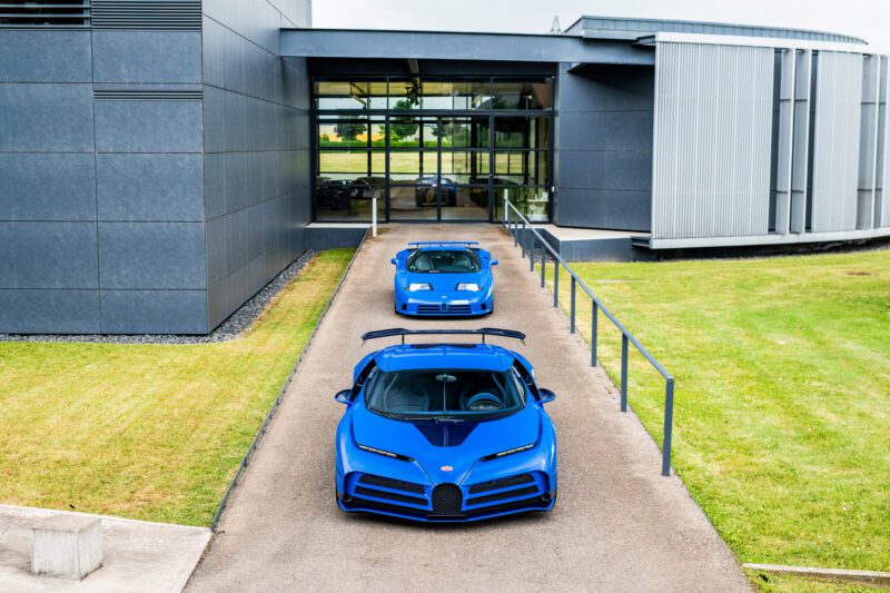 Three blue Bugatti sports cars, including a 1-of-39 ’90s hypercar royalty—the EB110 SS—are parked in a line on a driveway outside a modern building with large windows and metal siding.