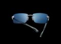 Rimless sunglasses with blue-tinted lenses, silver detailing, and partially folded translucent temples displayed on a black background—an elegant example of Tourbillon-Inspired Eyewear by Bugatti, ready for SILMO 2025.