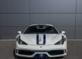 A stunning 2015 Ferrari 458 Speciale Aperta with blue racing stripes is parked in front of a gray metal wall, captured from the front—perfect for those seeking a Ferrari for sale.