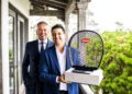 Two men in suits stand on a balcony; one holds a boxed Bugatti Automobiles item with a mesh front, celebrating the Best Performing Brand Manager at Bugatti Broward.