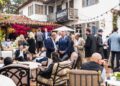 A group of people in formal and semi-formal attire socialize at an outdoor gathering on a patio with string lights and a Bugatti Broward banner in the background, celebrating with the Brand Manager at this exclusive 2024 event.