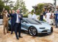 Abraham Cohen, Best Performing Brand Manager at Bugatti Broward, speaks into a microphone beside a blue Bugatti sports car, addressing the crowd at an outdoor event.