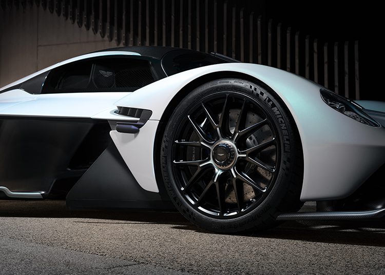 Close-up side view of a sleek white sports car, reminiscent of an Aston Martin Valkyrie, featuring large black alloy wheels with Michelin tires, photographed at night—ideal for Broad Arrow Auction enthusiasts.