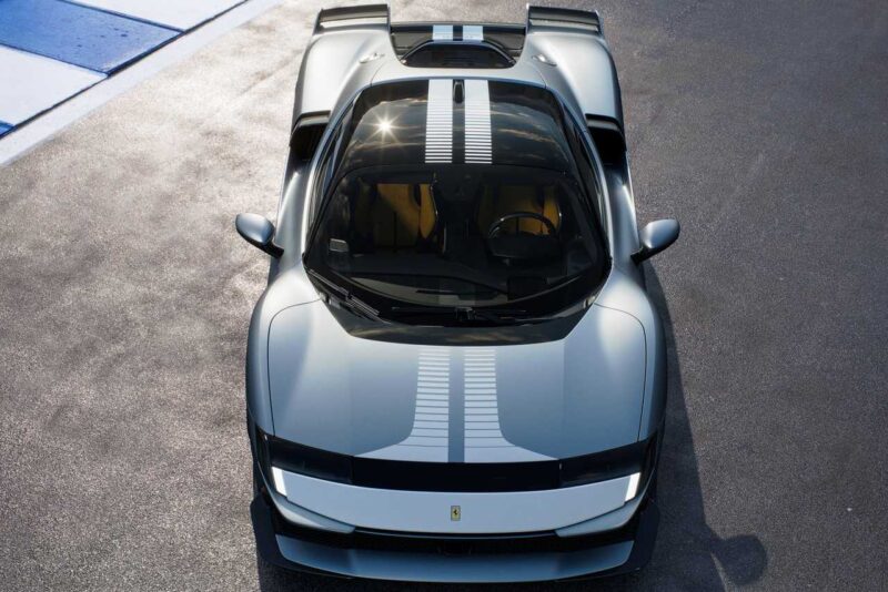 Overhead view of a silver sports car with white racing stripes, parked on asphalt next to a blue and white curb—perfect for a Comparison: Ferrari SF90 Stradale Vs. Ferrari 849 Testarossa showcase.