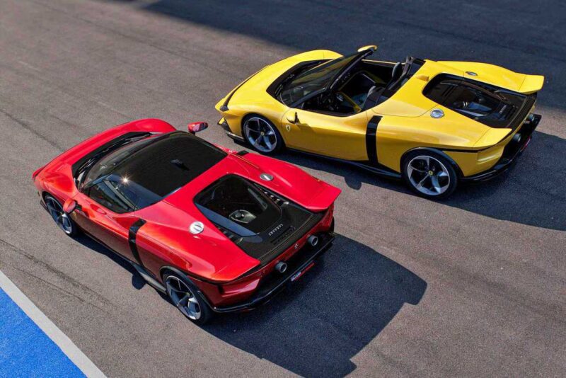 Two sports cars, a red Ferrari SF90 Stradale and a yellow Ferrari 849 Testarossa, are parked side by side on a paved surface, viewed from above—a striking comparison of iconic design and performance.