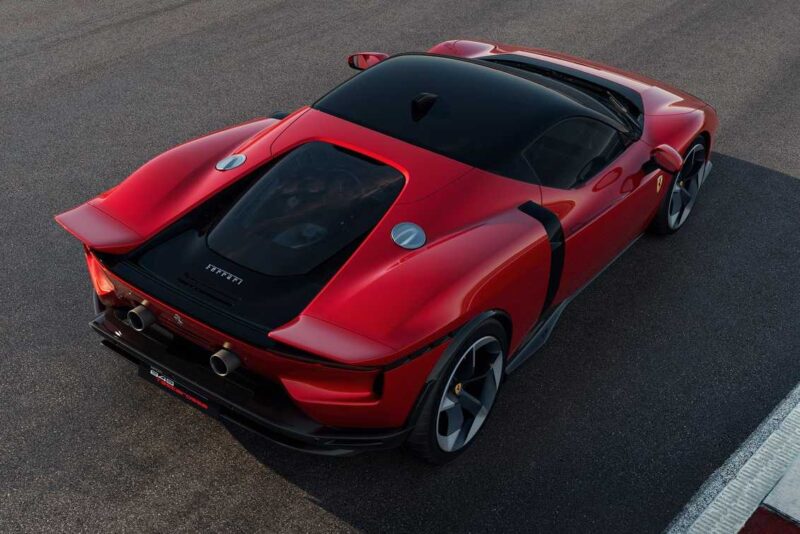 A red Ferrari sports car, reminiscent of the Comparison: Ferrari SF90 Stradale Vs. Ferrari 849 Testarossa, is parked on asphalt and viewed from above and behind, highlighting its aerodynamic design and sleek engine cover.