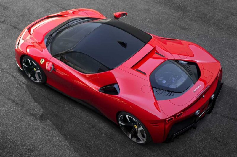 Aerial view of a red Ferrari sports car parked on a paved surface, showcasing its sleek design and black roof—perfect for a Comparison: Ferrari SF90 Stradale Vs. Ferrari 849 Testarossa.