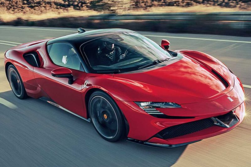 A red sports car, reminiscent of the Ferrari SF90 Stradale Vs. Ferrari 849 Testarossa comparison, drives on a road with a blurred background, highlighting its sleek aerodynamic design and a person seated inside.
