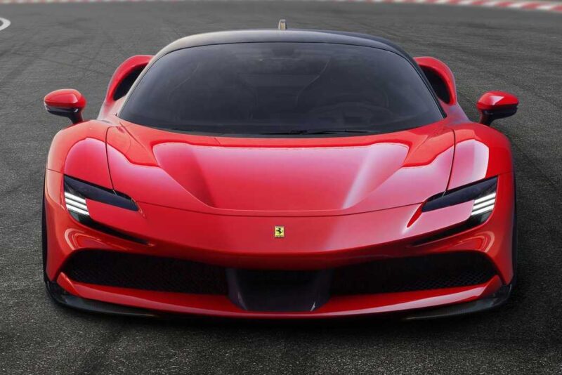 Front view of a red Ferrari SF90 Stradale parked on a racetrack, showcasing its sleek design, headlights, and iconic Ferrari logo—perfect for a Comparison: Ferrari SF90 Stradale Vs. Ferrari 849 Testarossa.