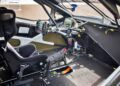 Interior of a race car, similar to those in Two Fords EVs Two Records: Lightning SuperTruck and SuperVan Conquer the Green Hell, showing a single racing seat, steering wheel with controls, display screens, and exposed wiring and components.
